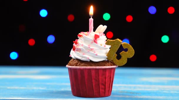 Delicious birthday cupcake with burning candle and number 13 on multicolored blurred lights background — Stock Video