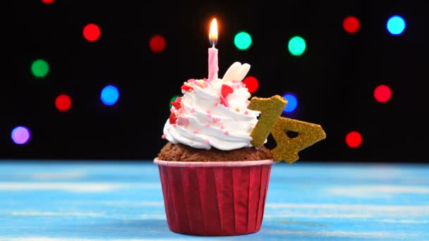 Вкусный праздничный кекс с горящей свечой и номер 14 на многоцветном фоне размытых огней — стоковое видео