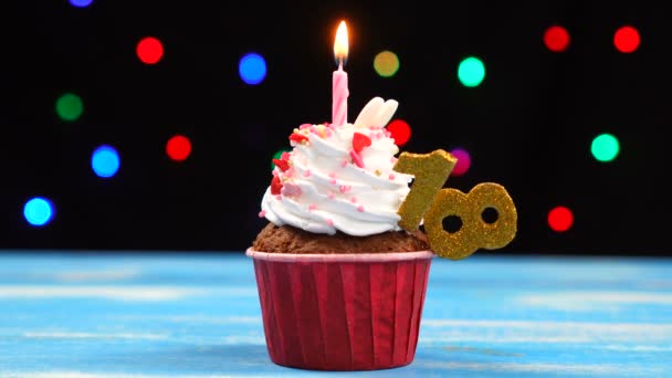 Delicious birthday cupcake with burning candle and number 18 on multicolored blurred lights background — Stock Video