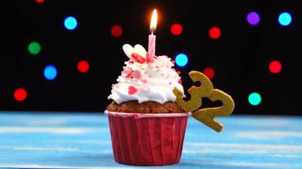 Смачний кекс на день народження з палаючою свічкою та No 32 на різнокольоровому тлі розмитих вогнів — стокове відео
