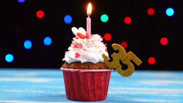 Delicious születésnapi Cupcake égő gyertyát, és a szám 35 a többszínű homályos fények háttér — Stock videók