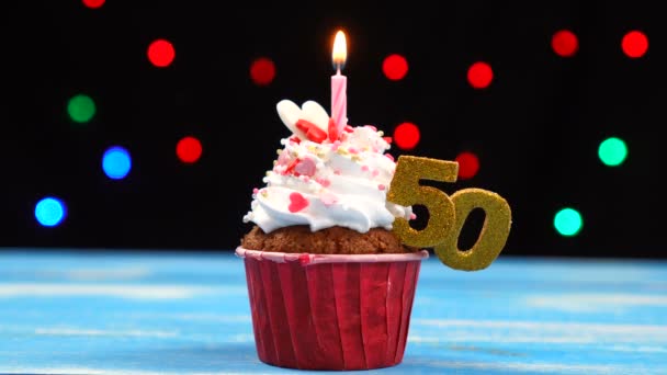 Вкусный праздничный кекс с горящей свечой и номер 50 на многоцветном фоне размытых огней — стоковое видео