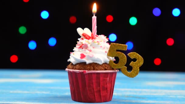 Вкусный праздничный кекс с горящей свечой и номер 53 на многоцветном фоне размытых огней — стоковое видео