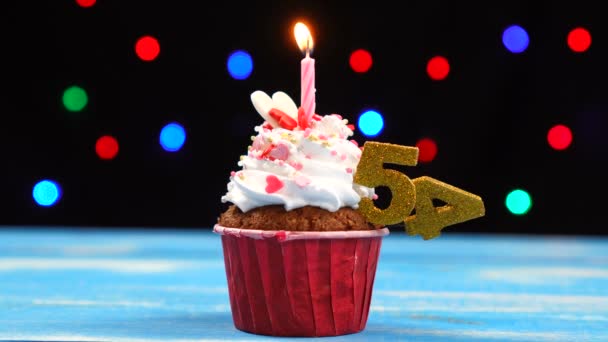 Delicious birthday cupcake with burning candle and number 54 on multicolored blurred lights background — Stock Video