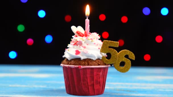 Delicious birthday cupcake with burning candle and number 56 on multicolored blurred lights background — Stock Video