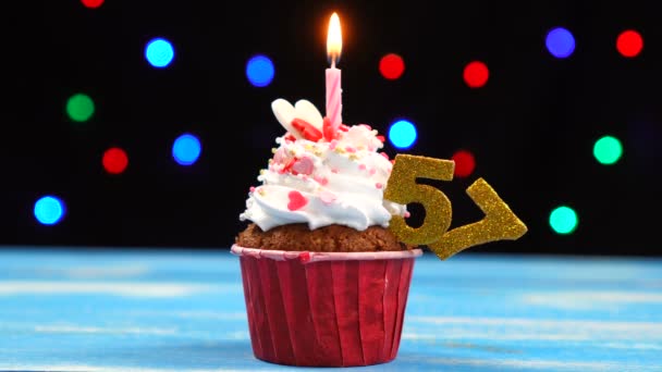 Вкусный праздничный кекс с горящей свечой и номер 57 на многоцветном фоне размытых огней — стоковое видео