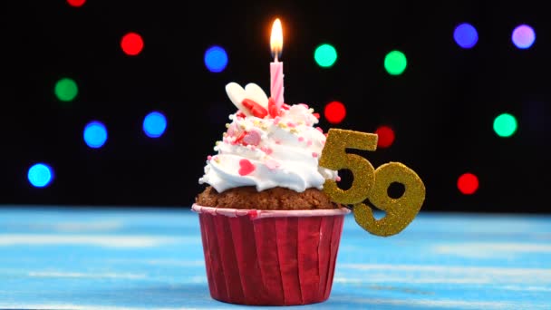 Výborný narozeninový dort s hořící svíčkou a číslo 59 na pozadí barevných rozmazaných světel — Stock video