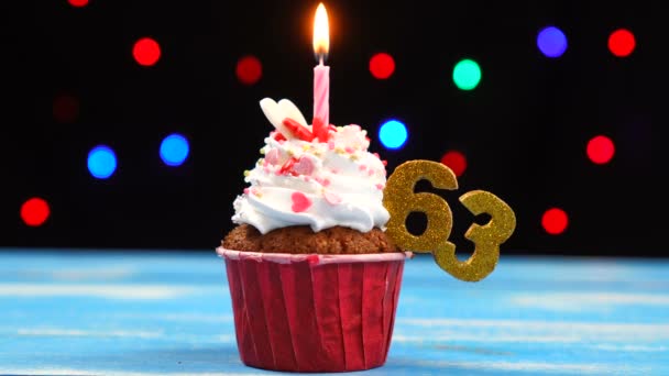 Výborný narozeninový dort s hořící svíčkou a číslo 63 na pozadí barevných rozmazaných světel — Stock video