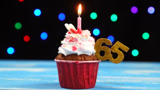 Läcker födelsedag cupcake med brinnande ljus och nummer 65 på mångfärgade dimstrålkastare bakgrund — Stockvideo