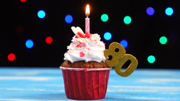Delicioso cupcake de cumpleaños con vela encendida y número 80 sobre fondo de luces borrosas multicolores — Vídeos de Stock