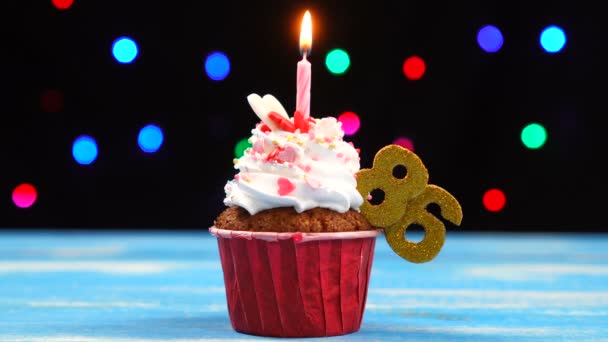 Delicious születésnapi Cupcake égő gyertyát, és a szám 86 a többszínű homályos fények háttér — Stock videók