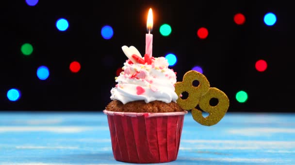Вкусный праздничный кекс с горящей свечой и номер 89 на многоцветном фоне размытых огней — стоковое видео