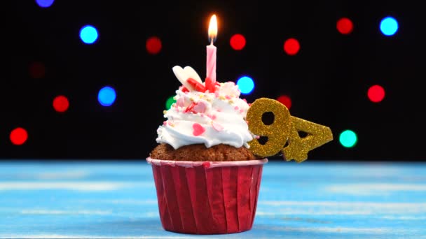 Delicioso cupcake de aniversário com vela acesa e número 94 em luzes borradas multicoloridas fundo — Vídeo de Stock