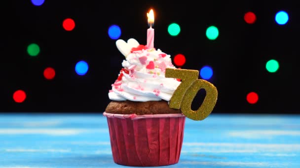 Delicious birthday cupcake with burning candle and number 70 on multicolored blurred lights background — Stock Video