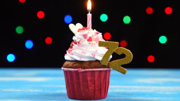 Delicious birthday cupcake with burning candle and number 72 on multicolored blurred lights background — Stock Video