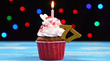 Çok renkli bulanık ışıklar arka planda yanan mum ve sayı 77 ile Lezzetli doğum günü cupcake