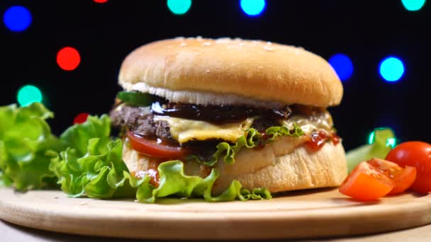 Hamburguesa casera y fresca sabrosa con queso, tomate, lechuga sobre fondo de luces borrosas de colores — Vídeos de Stock