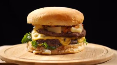 Siyah bir arka plan üzerinde ahşap tahta üzerinde dönen peynir, sos ve sebze ile büyük sulu hamburger