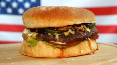 Amerikan Bayrağı önünde ahşap bir tahta üzerinde dönen peynir, sos ve sebze ile Sığır sulu burger