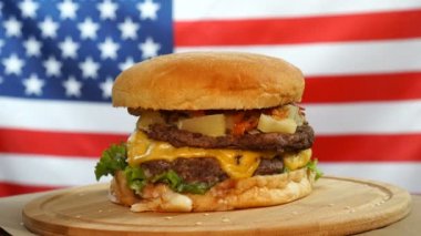 Peynir, sos ve sebze bize bayrak arka plan üzerinde ahşap bir tahta üzerinde dönen taze sulu burger.