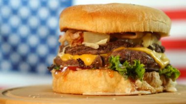 Amerikan Bayrağı önünde ahşap bir tahta üzerinde dönen peynir, sos ve sebze ile Sığır sulu burger