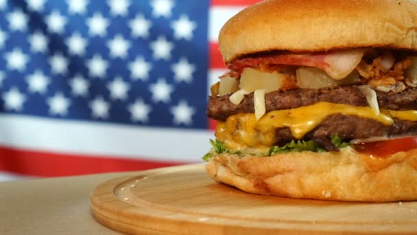 Verse sappige hamburger met kaas, saus en groenten draaiend op een houten bord voor de Amerikaanse vlag — Stockvideo