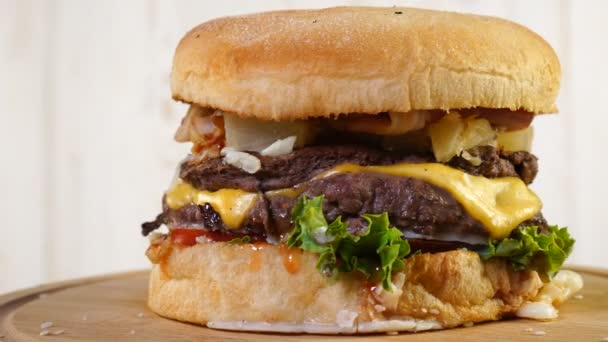 Сочный говяжий бургер с сыром, соусом и овощами, вращающимися на деревянной доске на белом фоне — стоковое видео