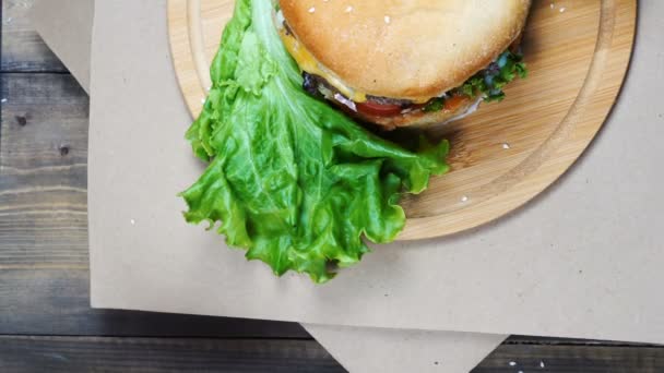 Vista superior de hamburguesa jugosa fresca con queso, salsa y verduras girando sobre una mesa de madera — Vídeos de Stock