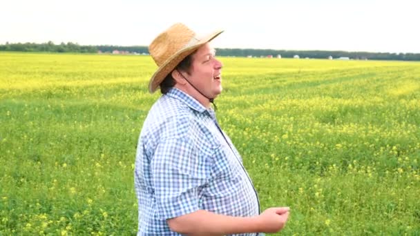 Retrato de un agricultor varón parado en un suelo agrícola fértil, mirando a la distancia e invitando a alguien — Vídeo de stock