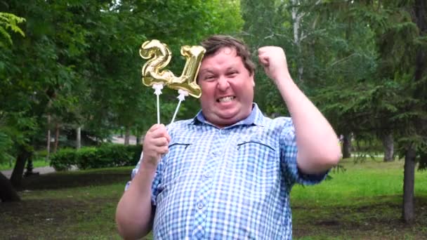 Hombre grande sosteniendo globos dorados haciendo el 21 número al aire libre. 21º aniversario fiesta de celebración — Vídeo de stock