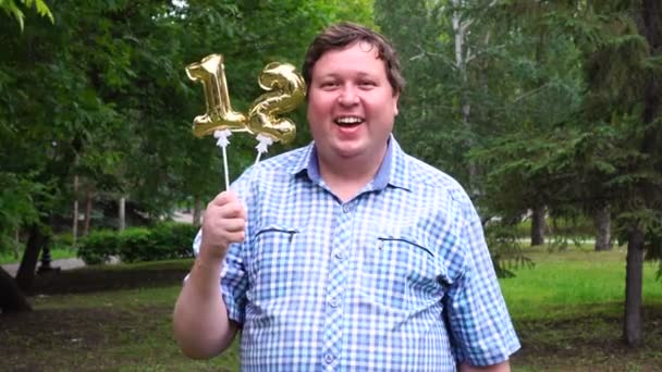 Grande homem segurando balões dourados fazendo o 12 número ao ar livre. 12th aniversário festa de celebração — Vídeo de Stock