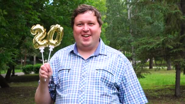 Hombre grande sosteniendo globos dorados haciendo el número 20 al aire libre. Fiesta de celebración del 20 aniversario — Vídeo de stock