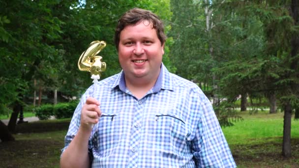 Big man Holding gouden ballon maken van de 4 nummer buiten. 4e verjaardag feest — Stockvideo