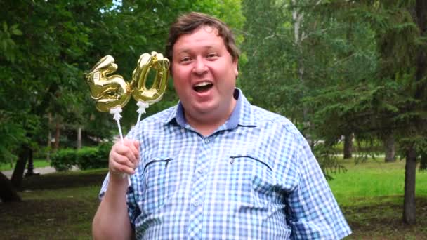 Μεγάλος άνθρωπος κρατώντας χρυσά μπαλόνια κάνοντας τον αριθμό 50 υπαίθριο. 50 η επέτειος Κόμμα εορτασμού — Αρχείο Βίντεο