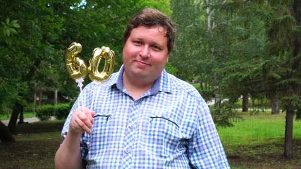 Hombre grande sosteniendo globos dorados haciendo el número 60 al aire libre. Fiesta de celebración del 60º aniversario — Vídeos de Stock