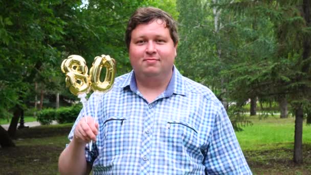 Big man innehar gyllene ballonger gör 80 nummer utomhus. 80-års jubileum fest — Stockvideo