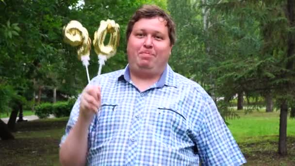 Big man innehar gyllene ballonger gör 90 nummer utomhus. 90-års jubileum fest — Stockvideo
