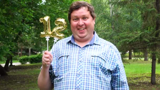 Μεγάλος άνθρωπος κρατώντας χρυσά μπαλόνια, φτιάχνοντας τον 12ο αριθμό έξω. 12th επέτειος πάρτι εορτασμού — Αρχείο Βίντεο