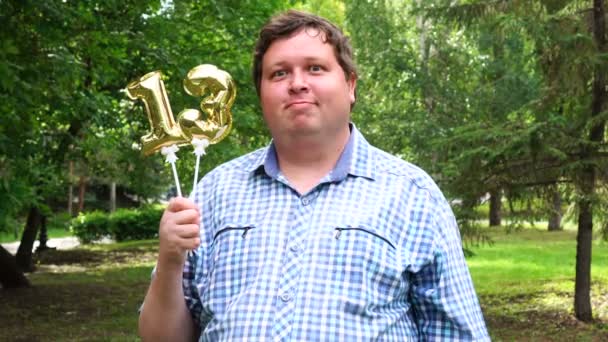 Big man holding golden balloons making the 13 number outdoor. 13th anniversary celebration party — Stock Video