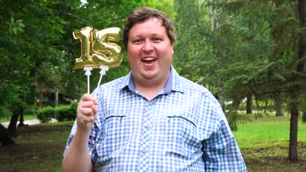 Großer Mann mit goldenen Luftballons, die die Zahl 15 im Freien bilden. Feier zum 16. Jahrestag — Stockvideo