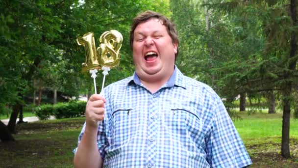 Большой человек с золотыми шариками делает 18 номеров на открытом воздухе. Празднование 18-летия — стоковое видео