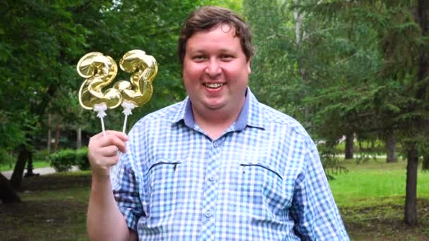 金色の風船を持った大男が23番を屋外に作る。23周年記念祝賀会 — ストック動画