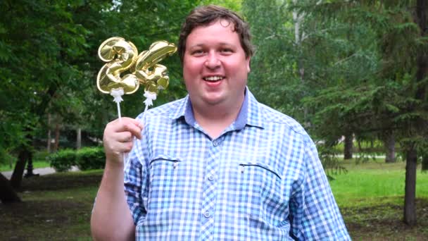 Velký muž, který drží zlaté balónky, dělá 24 čísel venku. 24tý výročí oslavy — Stock video