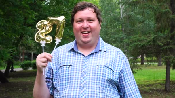 Big man innehar gyllene ballonger gör 27 nummer utomhus. 27-års jubileum fest — Stockvideo