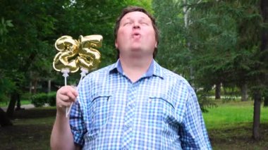 Elinde altın balonlar olan büyük adam 25 numarayı dışarıda yapıyor. 25. yıldönümü kutlama partisi