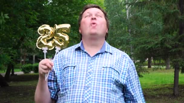 Grande homem segurando balões dourados fazendo o 25 número ao ar livre. Festa de celebração de 25 anos — Vídeo de Stock
