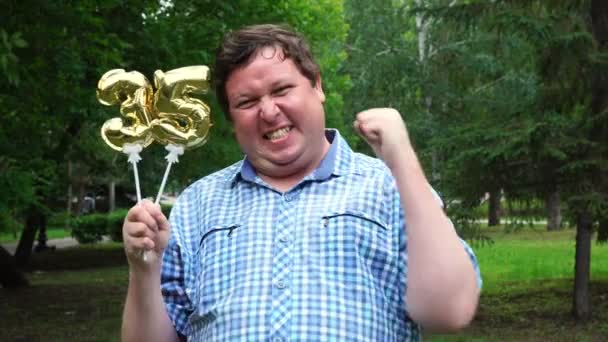 Μεγάλος άνθρωπος κρατώντας χρυσά μπαλόνια κάνοντας τον αριθμό 35 υπαίθριο. 35 η επέτειος πάρτι εορτασμού — Αρχείο Βίντεο
