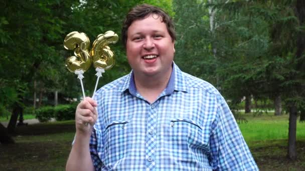 Hombre grande sosteniendo globos dorados haciendo el 36 número al aire libre. Fiesta de celebración del 36º aniversario — Vídeo de stock