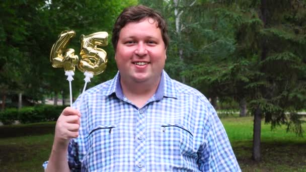 Великий чоловік тримає золоті кулі, що робить 45 номер відкритим. 45-річчя святкування вечірки — стокове відео