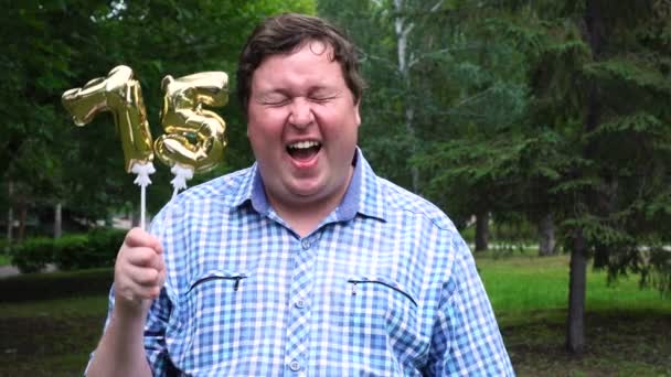 Großer Mann mit goldenen Luftballons, die die 75 Zahl im Freien machen. Feier zum 75-jährigen Bestehen — Stockvideo
